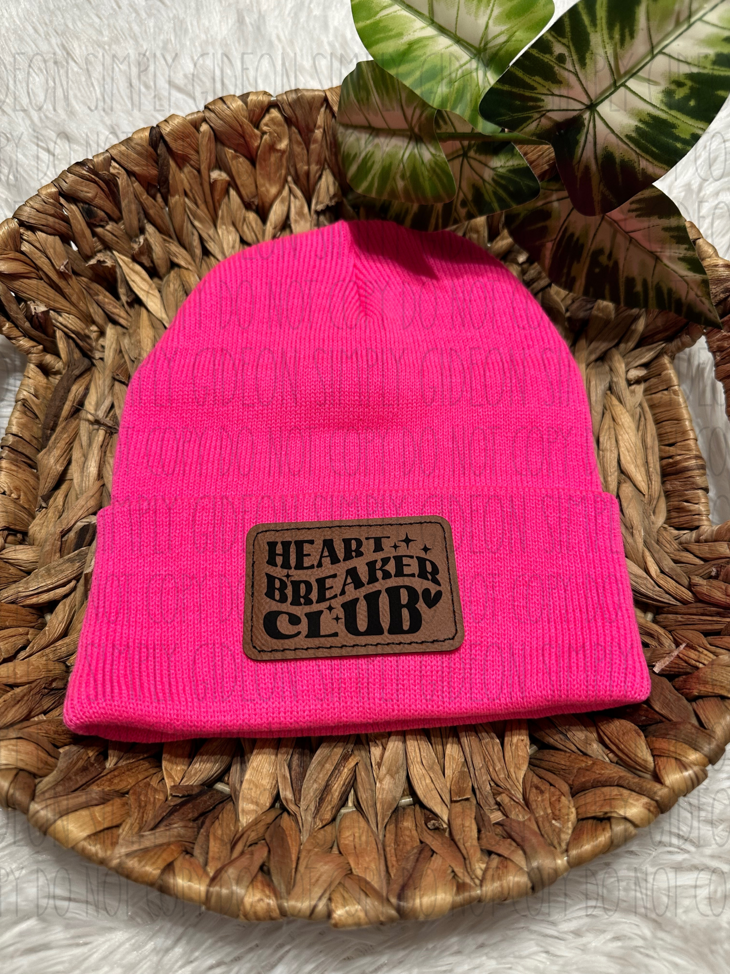 A neon pink acrylic beanie with a brown laser engraved patch that reads heart breaker club, with a heart and sparkles